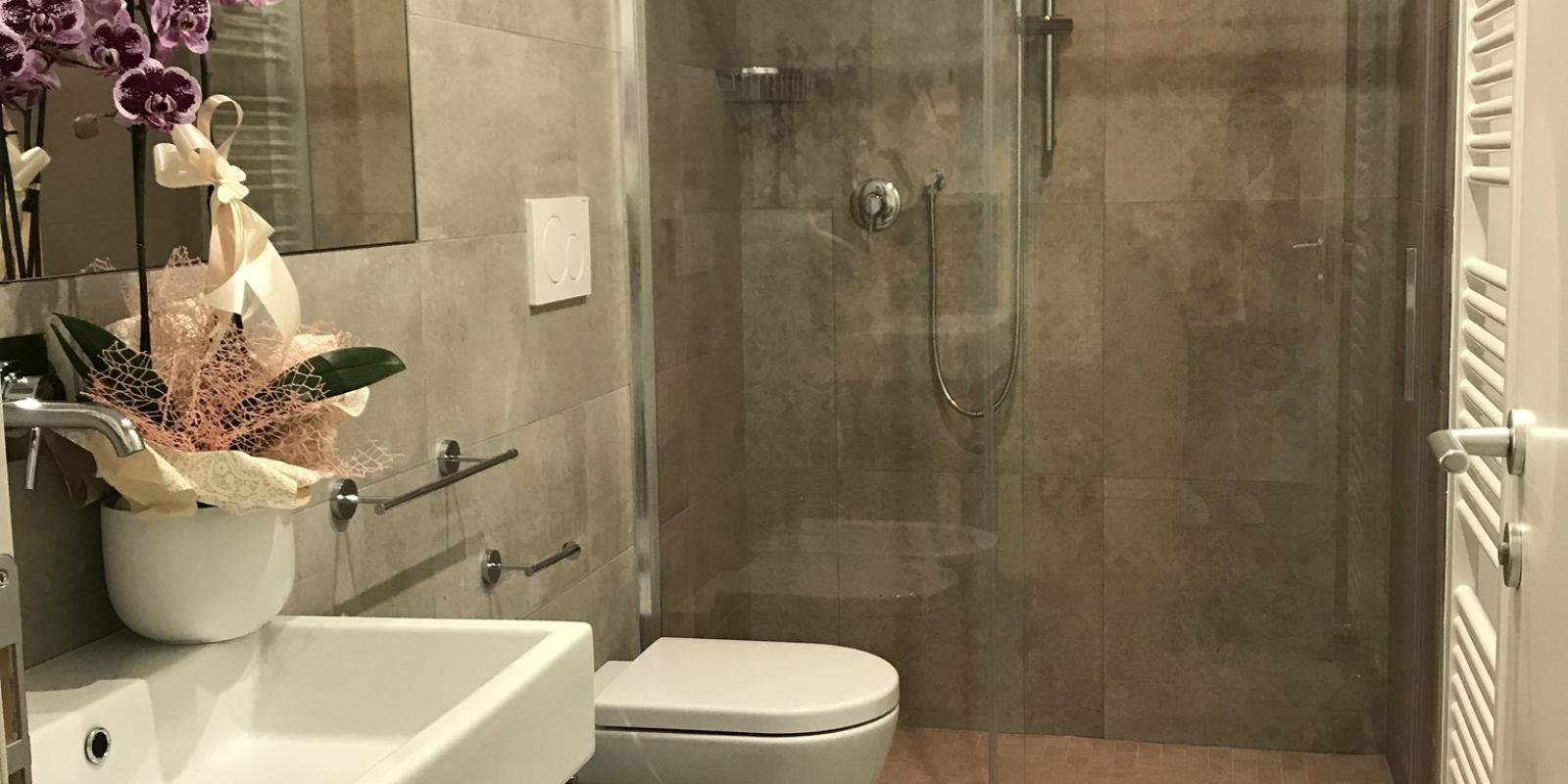 Bagno moderno con doccia in vetro, lavabo, bidet e decorazioni floreali.