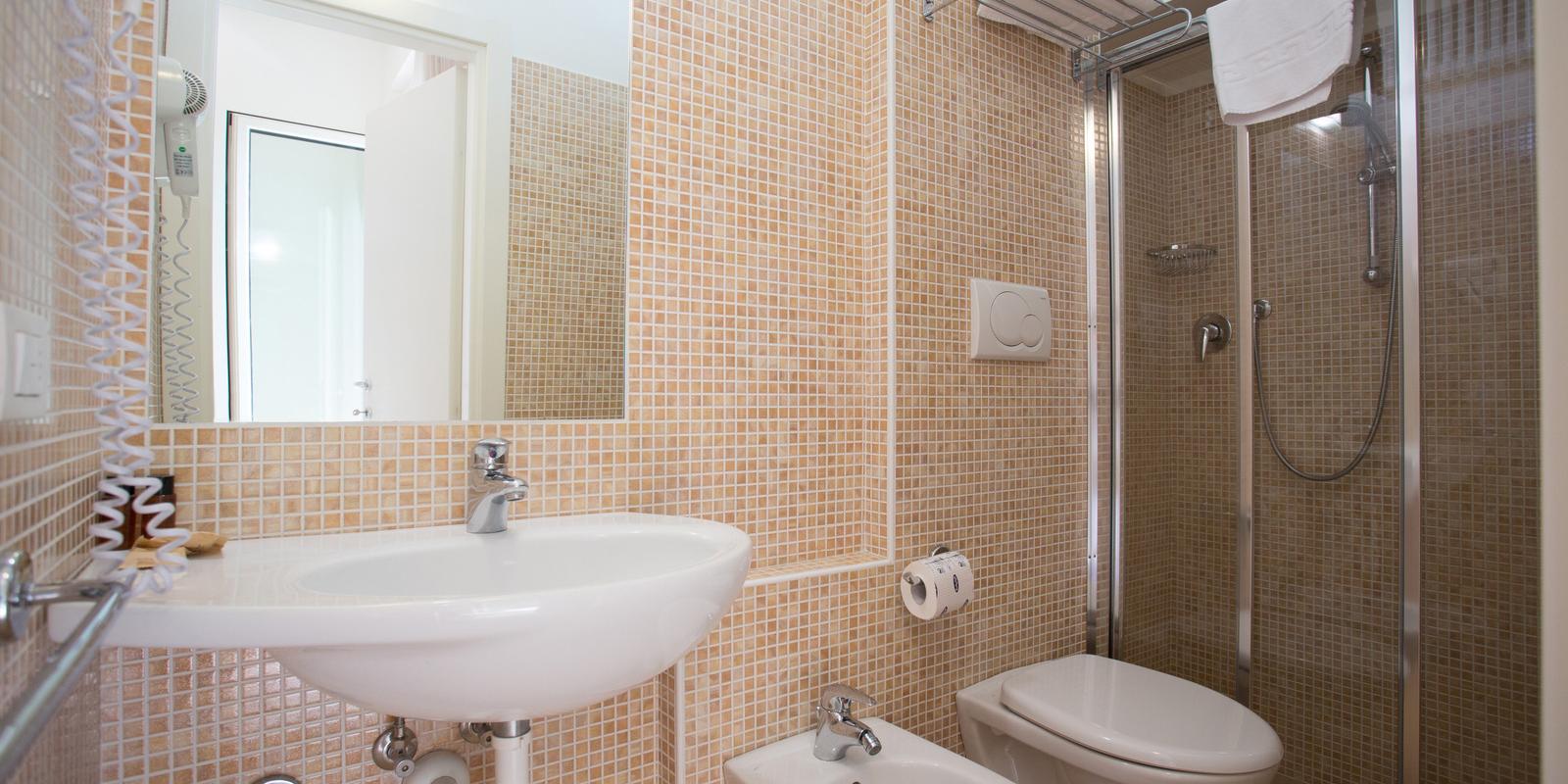 Bagno moderno con doccia, lavabo, bidet e WC, piastrelle beige e accessori bianchi.