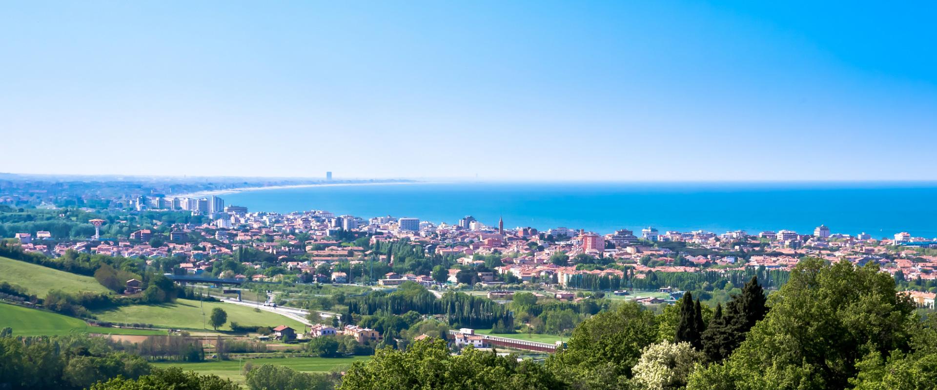 Panorama costiero con città, mare azzurro e colline verdi sotto un cielo limpido.