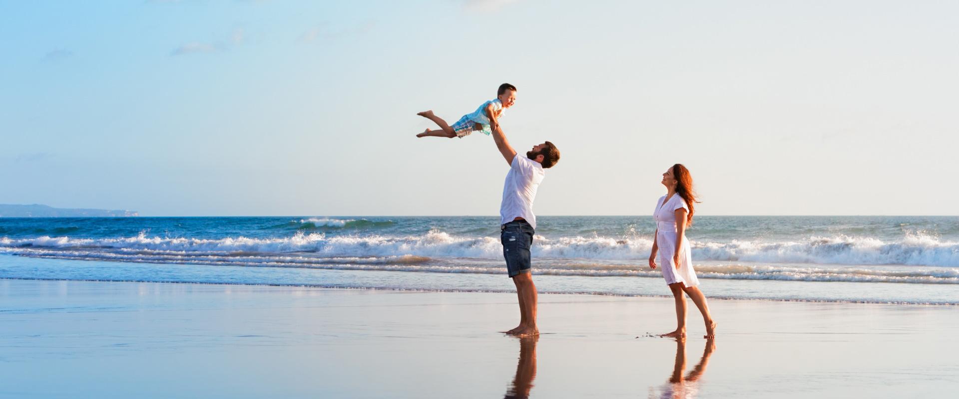 Famiglia felice gioca sulla spiaggia al tramonto, con onde sullo sfondo.