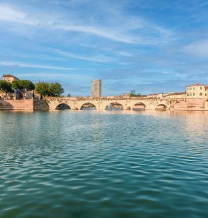 Ponte storico su un fiume con edifici e cielo azzurro sullo sfondo.