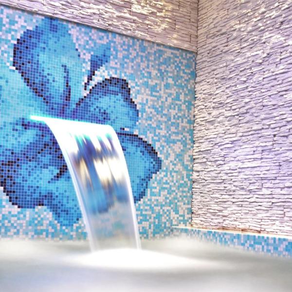 Blue mosaic with waterfall in pool.