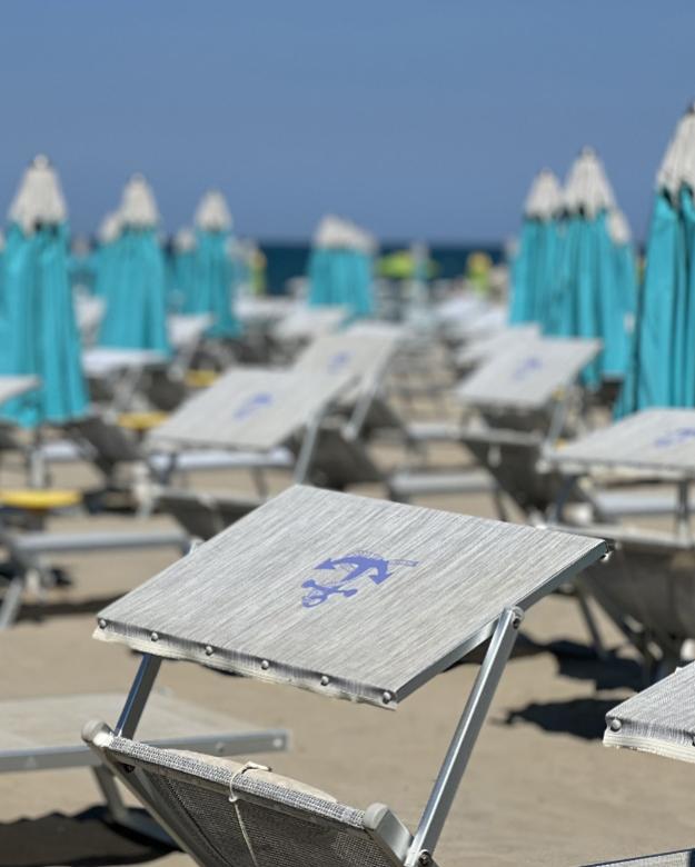 Spiaggia con lettini e ombrelloni azzurri chiusi, cielo sereno.