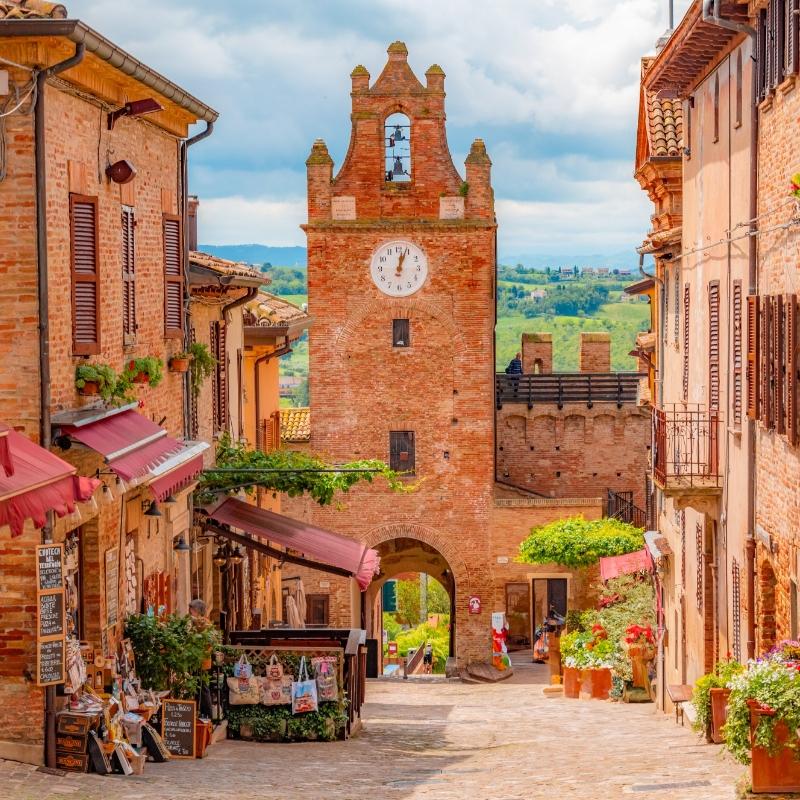 Stradina pittoresca con torre dell'orologio e negozi in un borgo italiano.