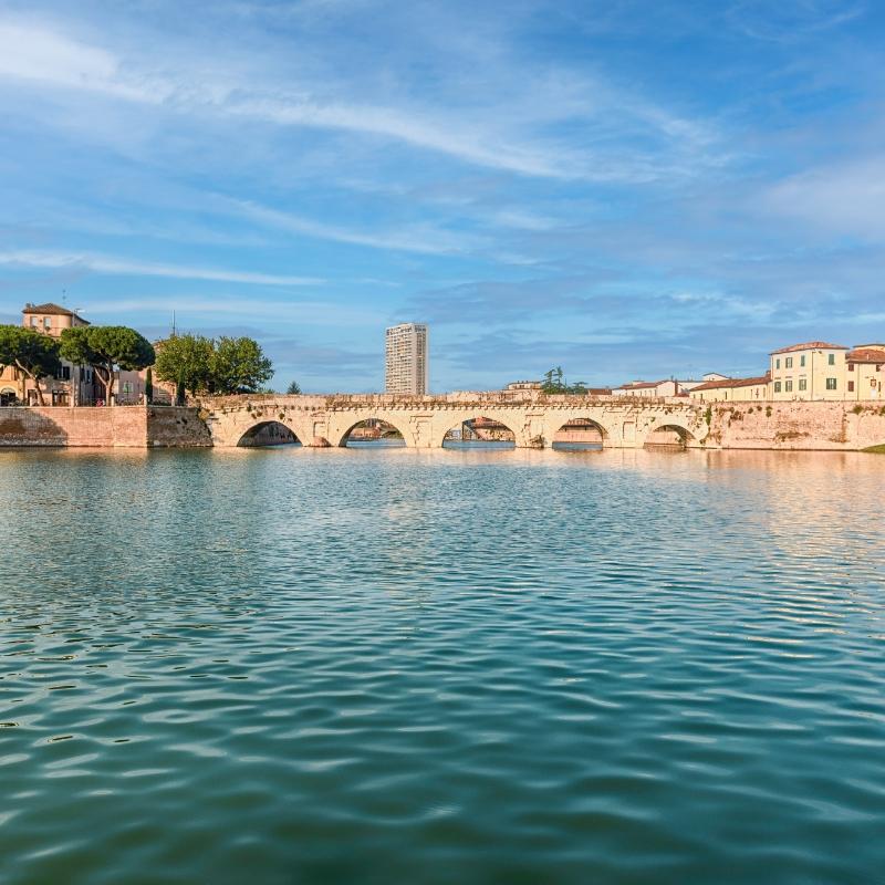 Ponte romano su un fiume con edifici e un cielo sereno.