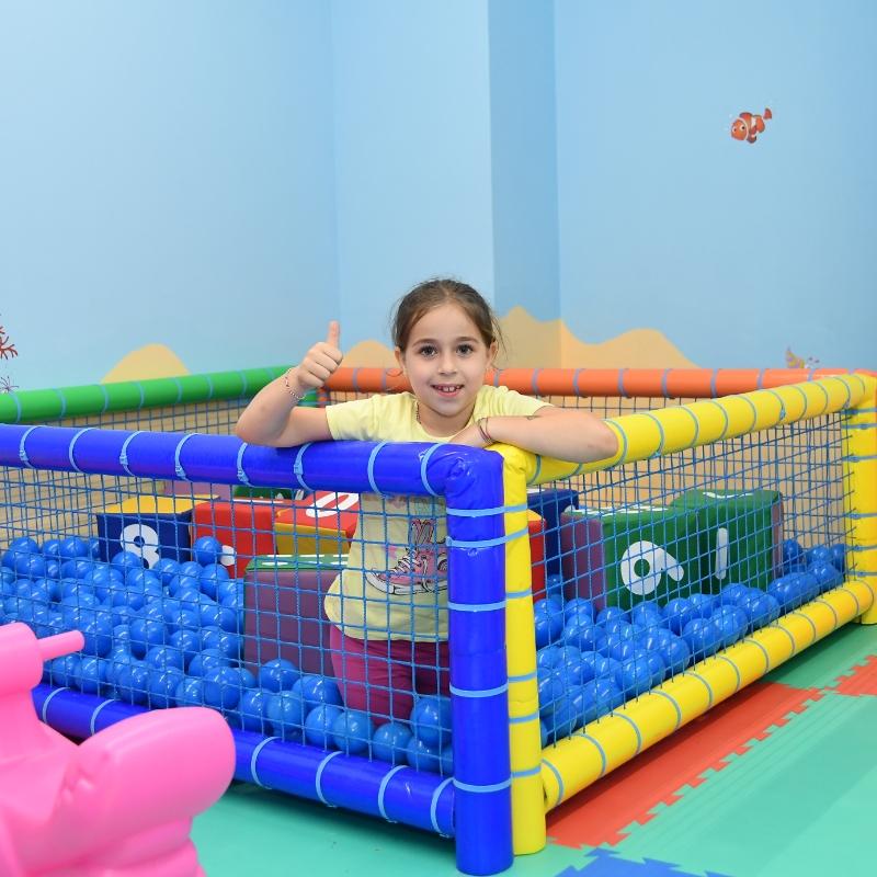 Bambina felice in un'area giochi con palline blu e pareti colorate.