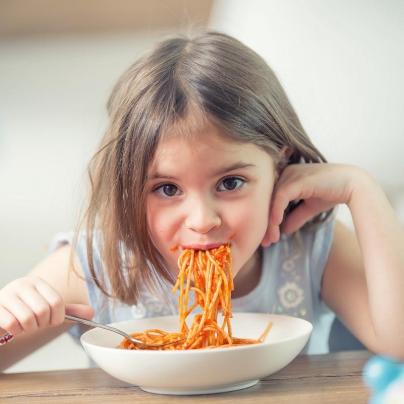 Bambina mangia spaghetti con gusto da un piatto bianco.