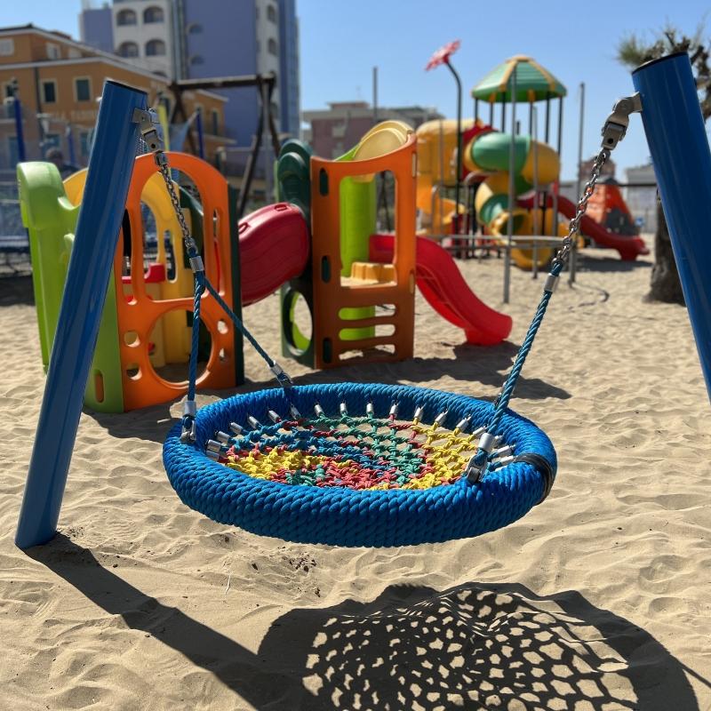 Parco giochi colorato con altalena a nido e scivoli su sabbia.