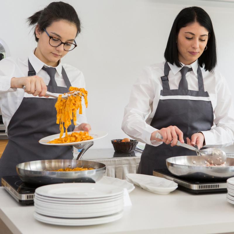 Due chef servono pasta in una cucina professionale.