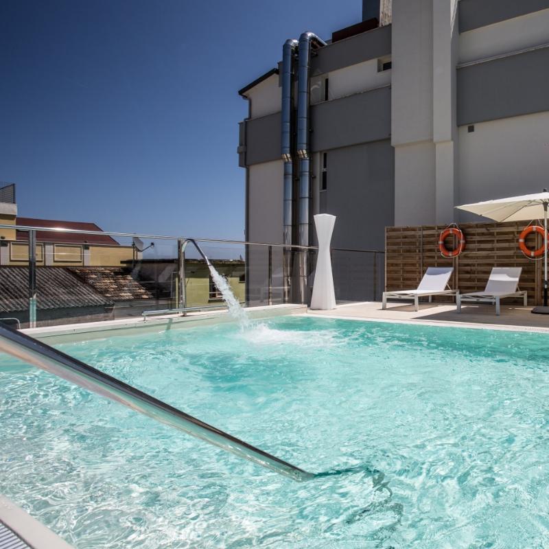 Piscina moderna su terrazza con lettini, ombrelloni e vista urbana.