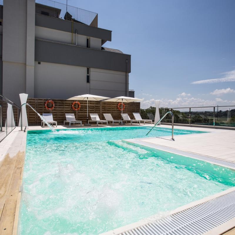 Piscina moderna con lettini e ombrelloni su una terrazza soleggiata.