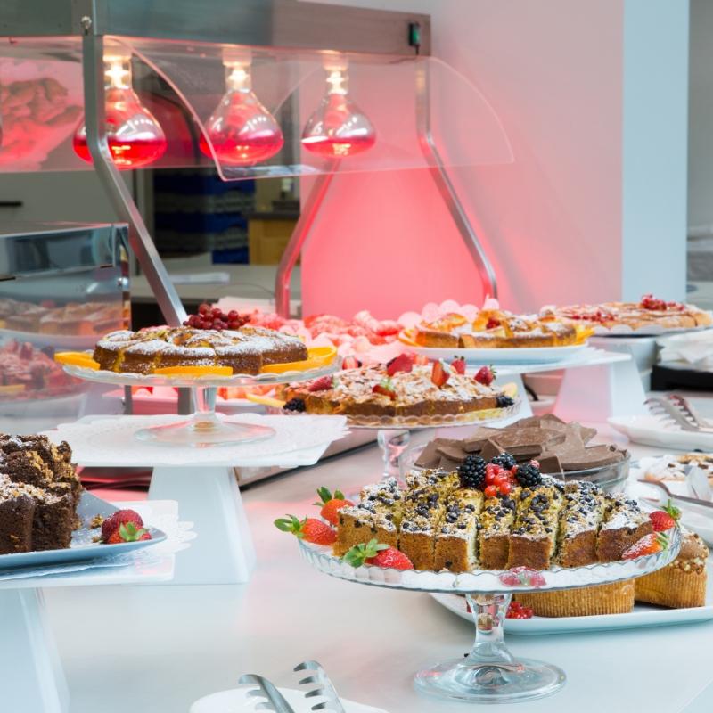 Buffet di dolci con torte e frutta sotto lampade riscaldanti.